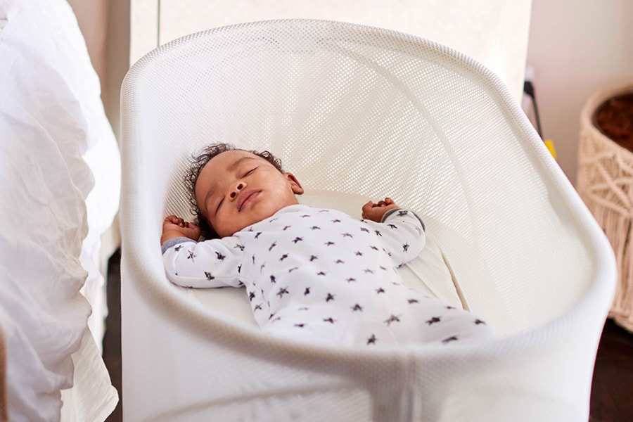 Infant sleeps on his back in a bassinet next to his parents’ bed