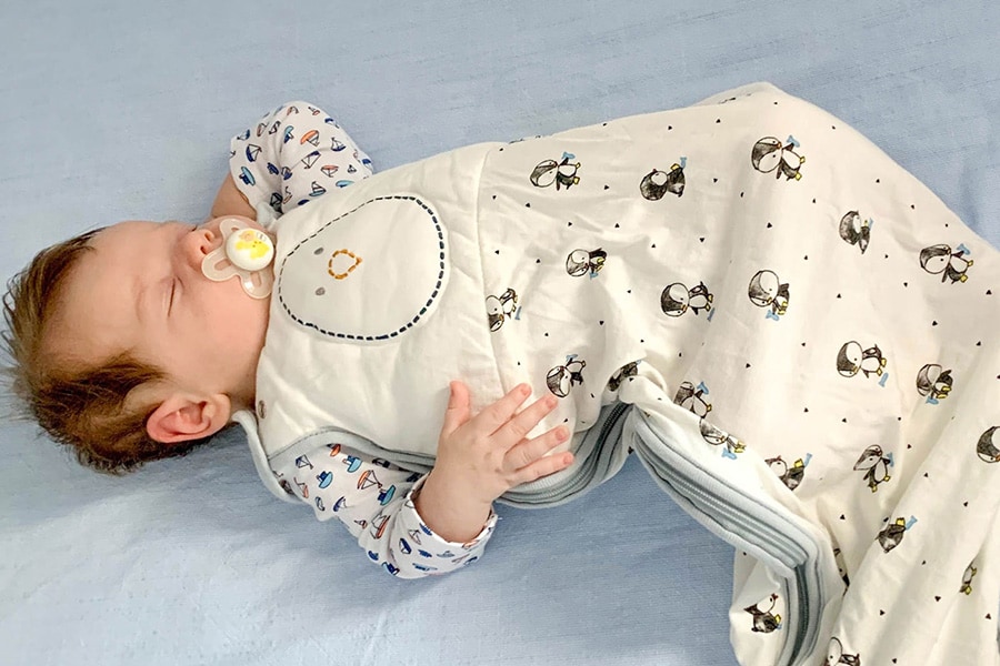 Infant wearing a sleep sack sleeps on his back in a clear crib