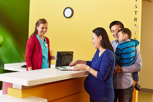 Pregnant mom, dad and toddler checking in for doctor's appointment at front desk