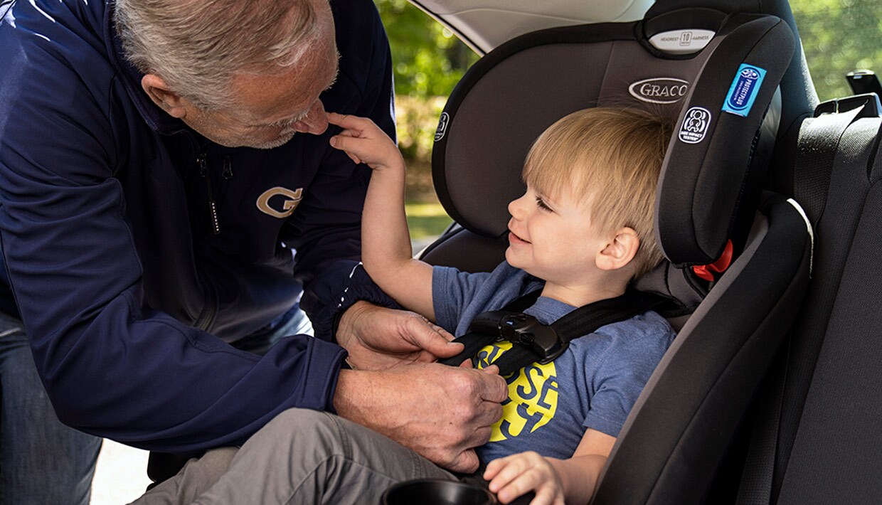 Grandpa securely buckling toddler into a forard-facing car seat
