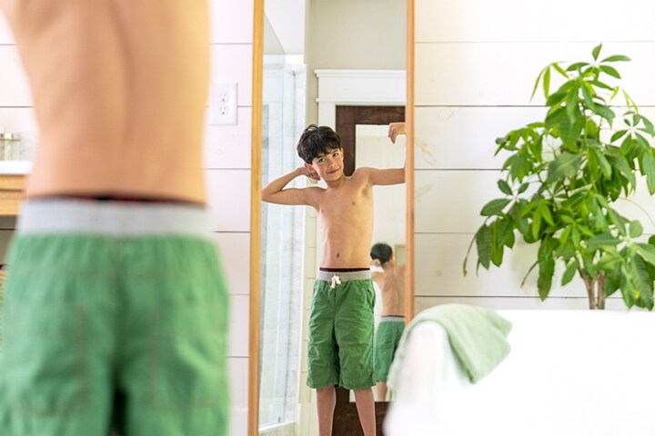Grade school boy flexing in mirror smiling