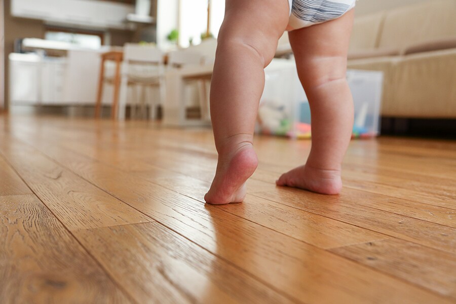 15-month-old toddler practices walking barefoot across a wooden floor.