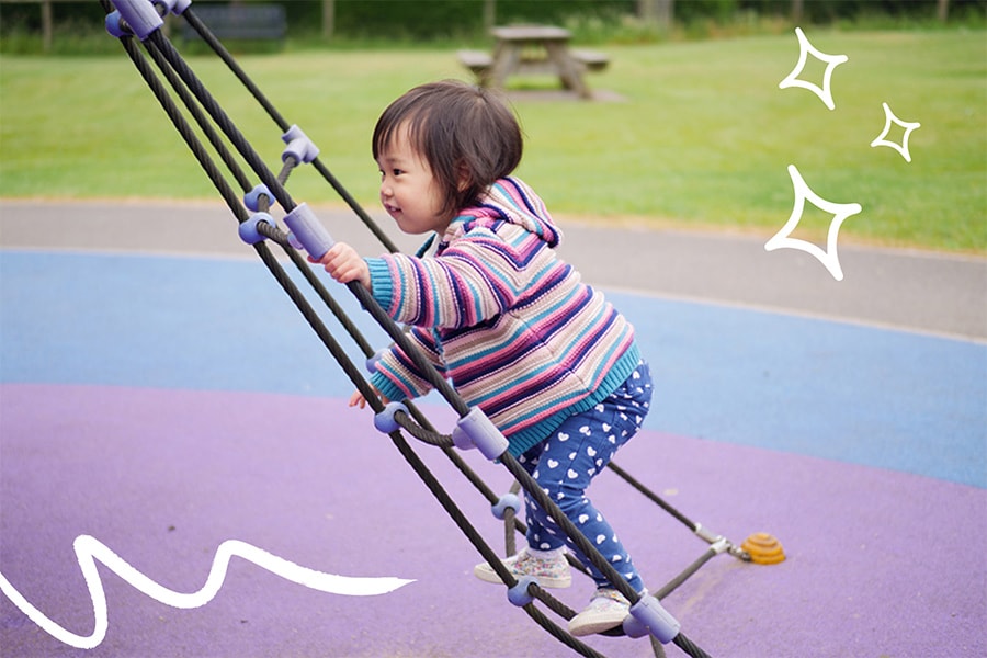 18-month-old toddler practices climbing on the playground
