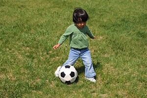 A toddler achieves the movement milestone of kicking a ball.