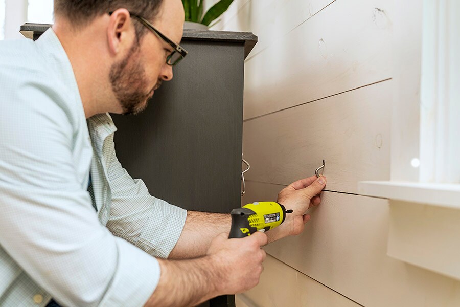 A parent practices proper home safety by securing a dresser to the wall with an anchor.