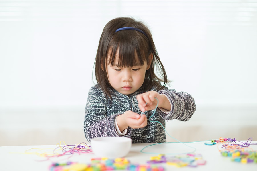 A 3-year-old develops their fine motor skills by stringing large beads together.