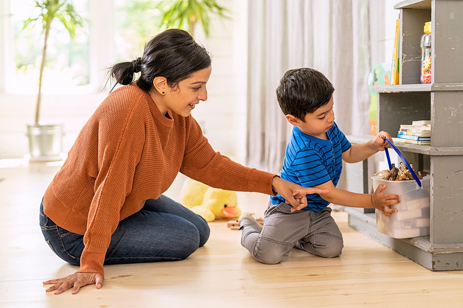 A parent and toddler place kid-safe items in an easy-to-access toy bin.