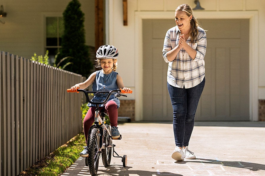 A parent cheers on their child, who safely rides a bike while wearing a helmet.