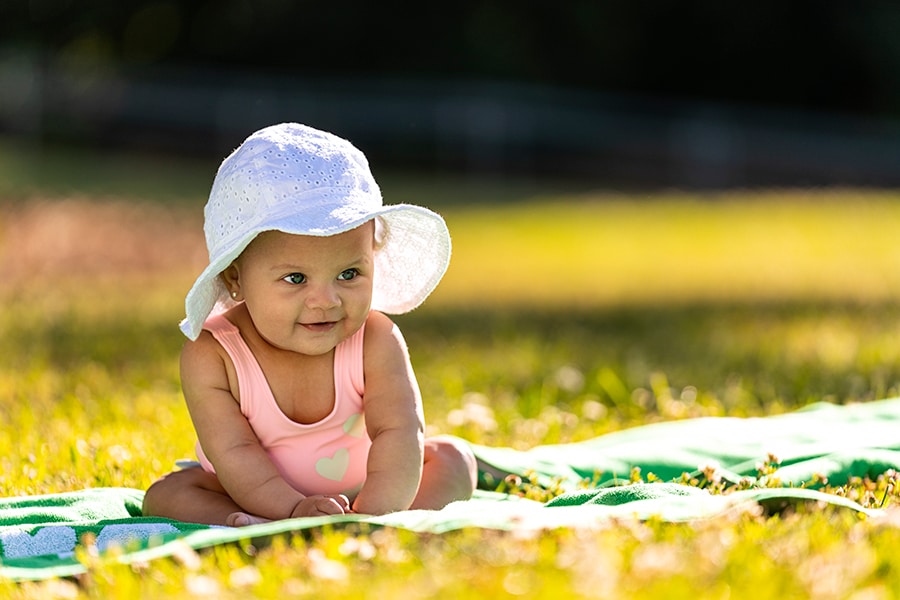 Baby is beginning to sit up on a towel at the park
