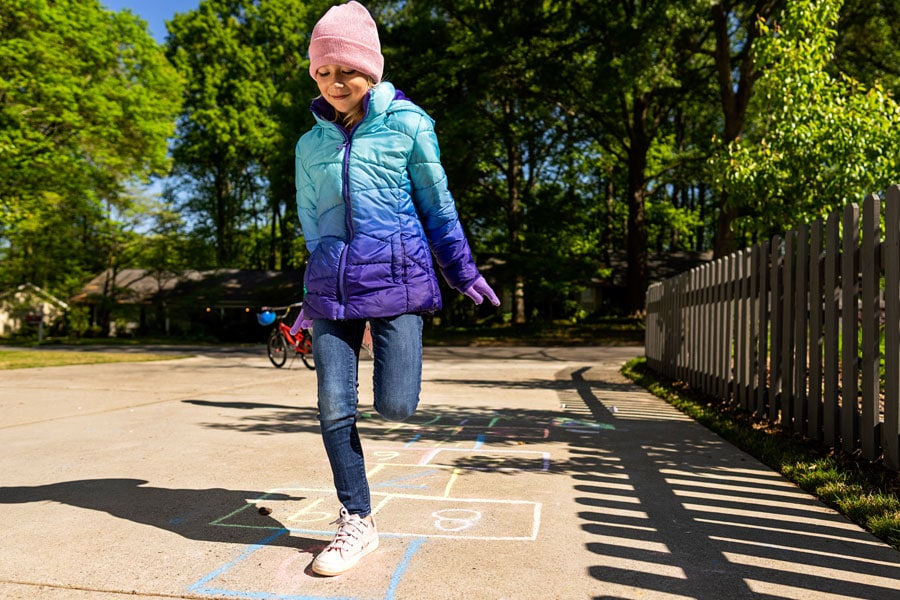 Elementary school-aged girl plays hopscotch outside, having fun being active.