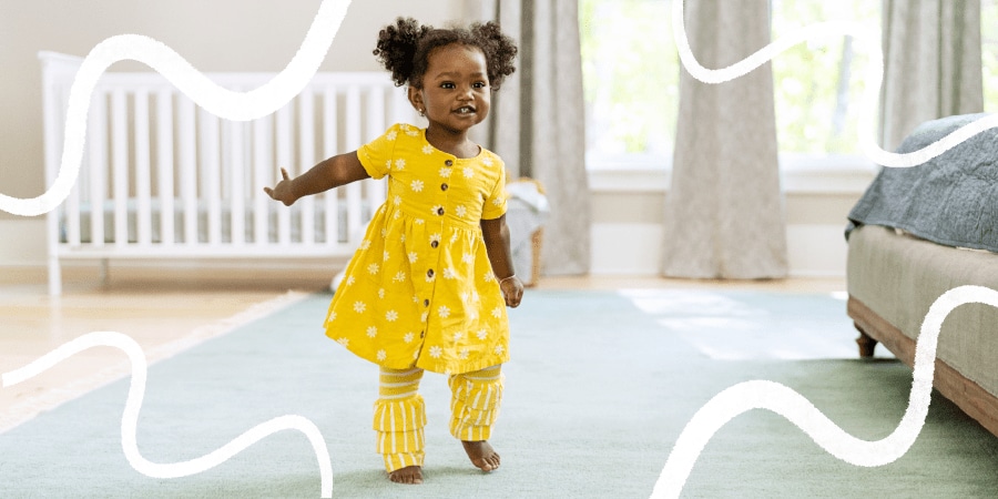 Toddler girl is smiling as she learns to walk, showing the benefits of physical activity for kids.