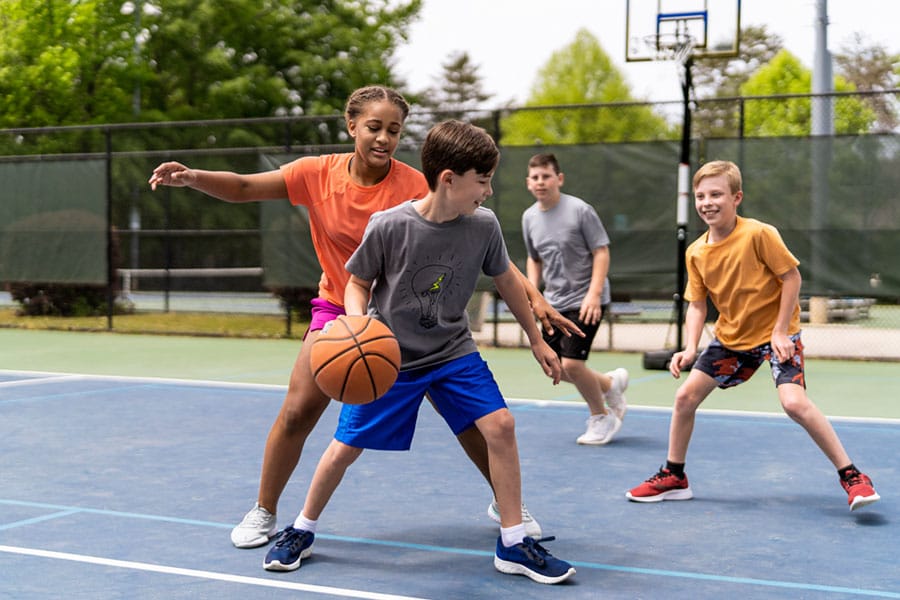 Elementary school-aged kids play pick-up basketball at the park, having fun being active. 