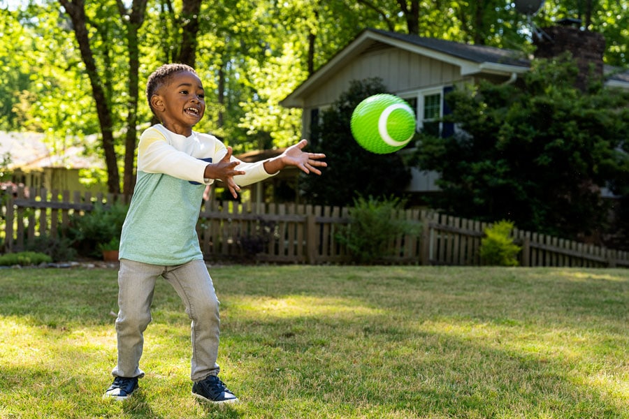 Toddler boy plays with a toy football outside, having fun being active.