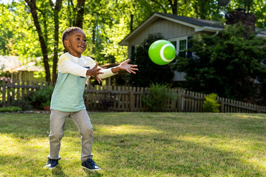 Toddler boy plays with a toy football outside, having fun being active. 