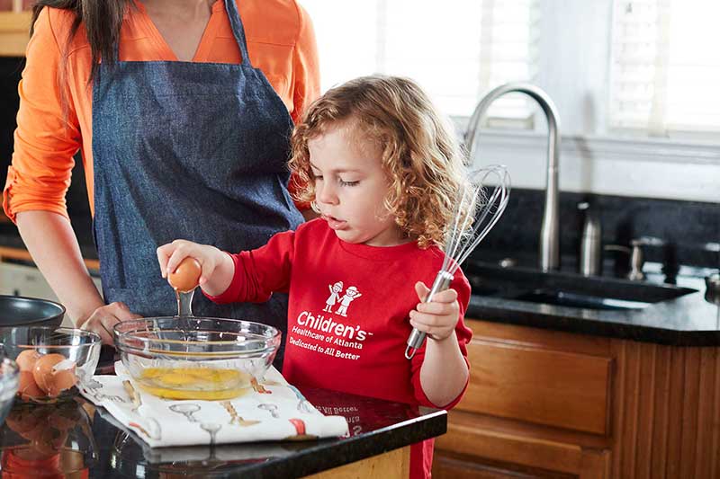 toddler cracking eggs into bowl