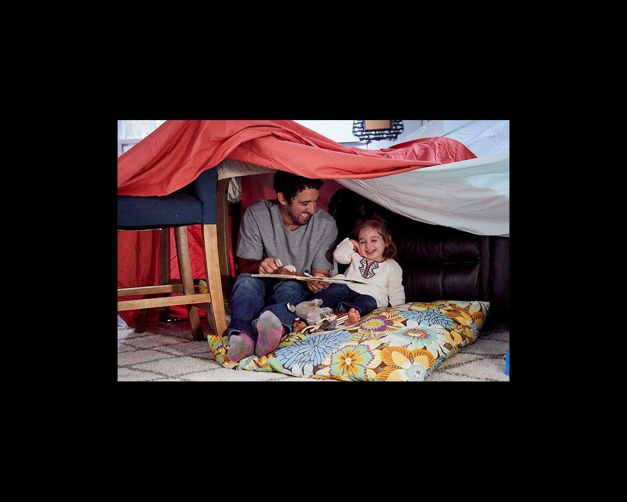 dad reading to toddler in blanket fort