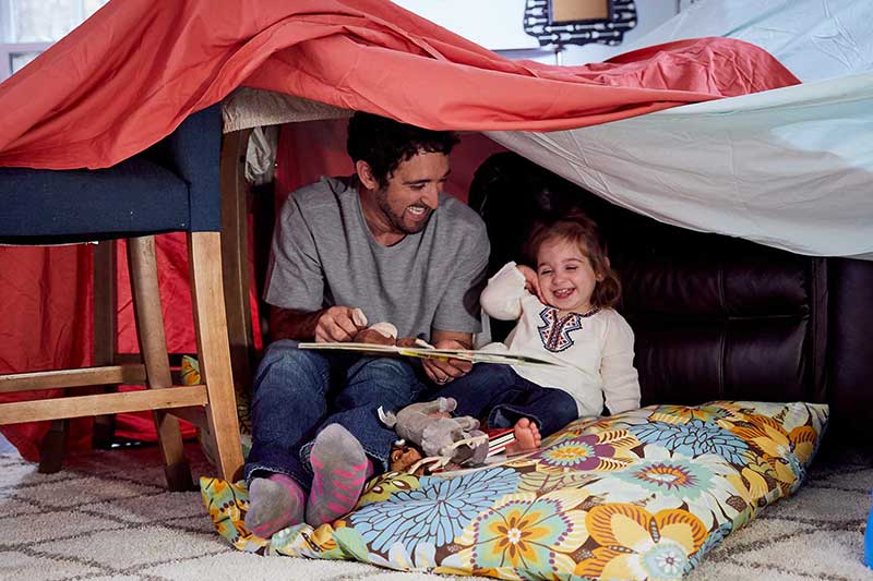 dad reading to toddler in blanket fort