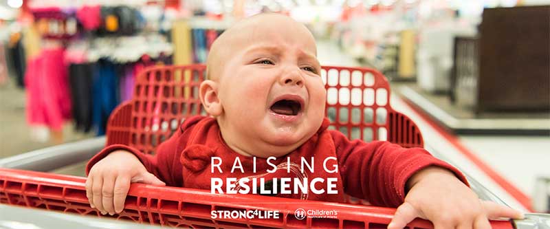 Infant crying in shopping cart with raising resilience logo overlaid