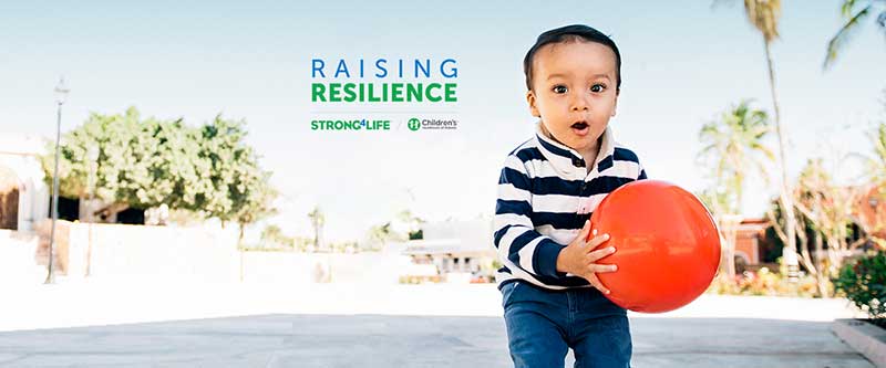 Toddler playing with red inflatable ball and raising resilience logo overlaid