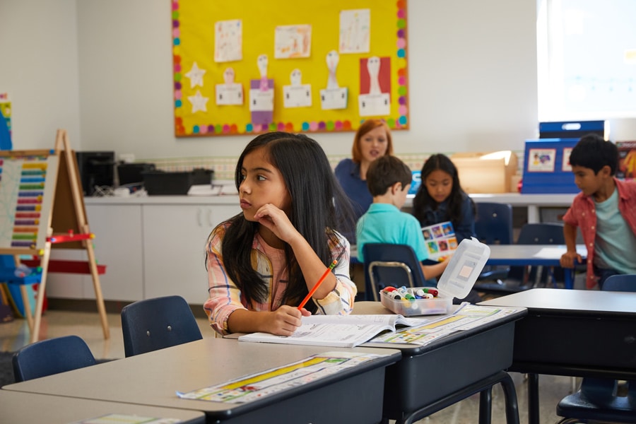 Young girl looks upset and distracted at school while away from classmates.