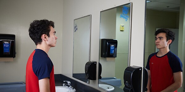 teen boy looking in mirror in school bathroom