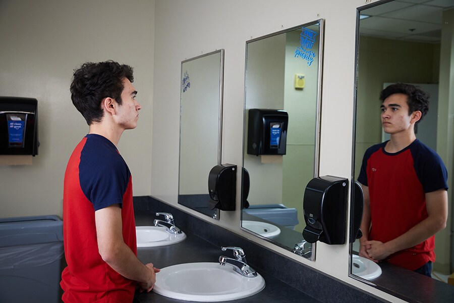 teen boy looking in mirror in school bathroom