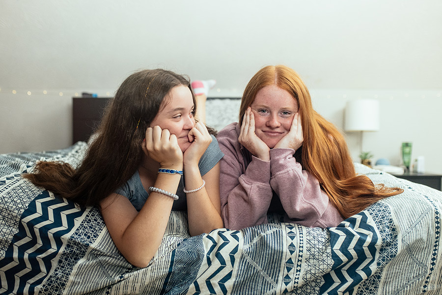 Younger sister looks adoringly at older sister in teen bedroom