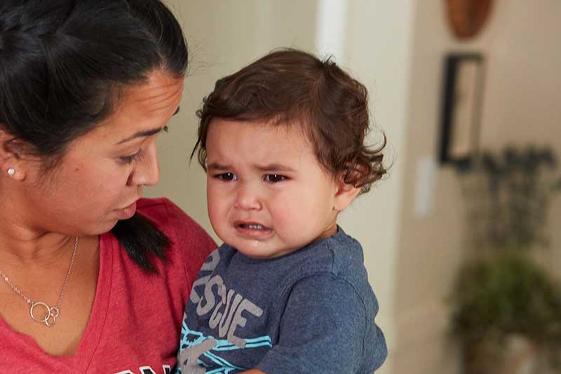 Mamá con un niño pequeño enojado y llorando en sus brazos