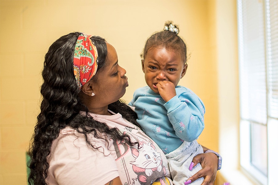 A photo of an adult woman calming down a crying toddler by holding her and talking to her