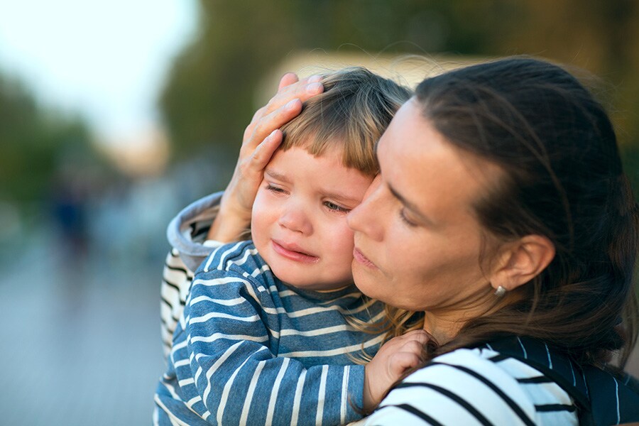 A mother comforting her overwhelmed toddler son outside with a hug.