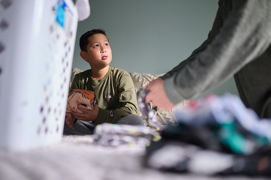 A middle school boy looks frustrated while folding laundry with his dad