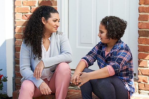 Mother and tween daughter talking outside of their house