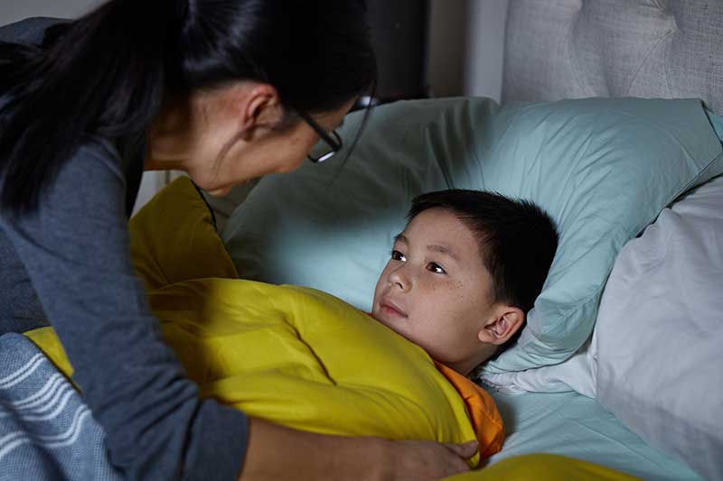 parent tucking boy into bed