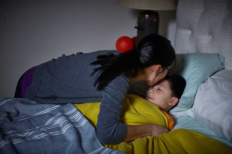 mom tucking son into bed