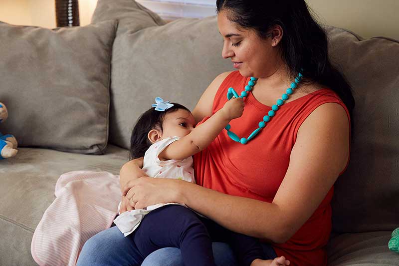 infant holding on to baby safe necklace while nursing