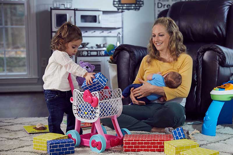 Mom nursing newborn while toddler plays