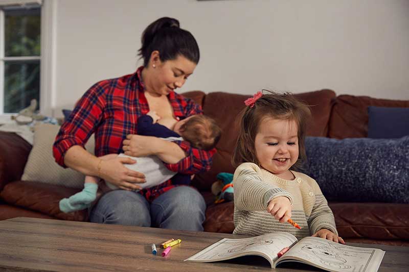 mom nursing newborn while toddler colors