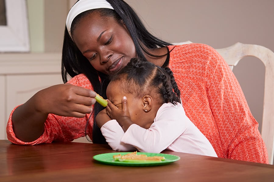 Toddler putting her hands over her face, refusing to eat because she is full. 