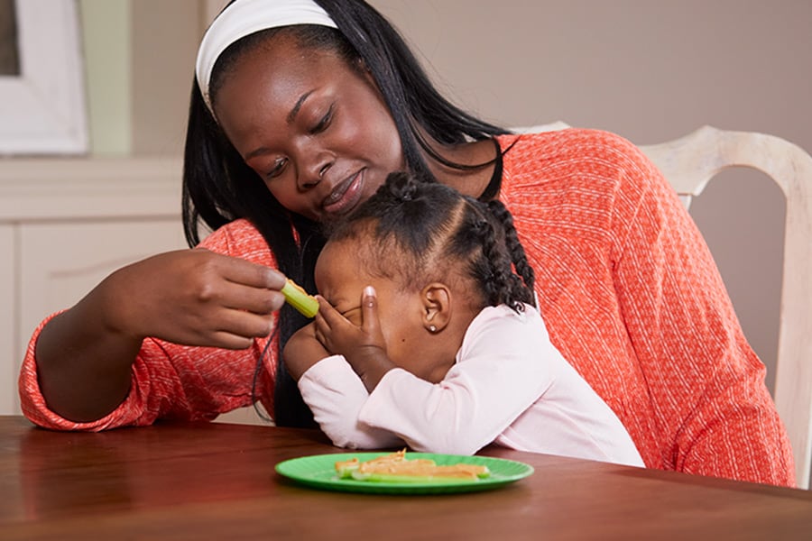 Toddler putting her hands over her face, refusing to eat because she is full.
