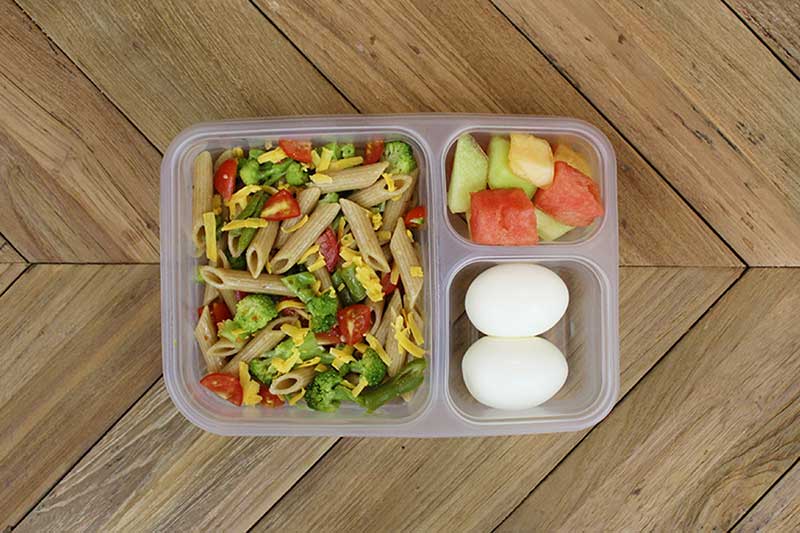 School packed lunch with veggie pasta salad, melon and hard-boiled eggs