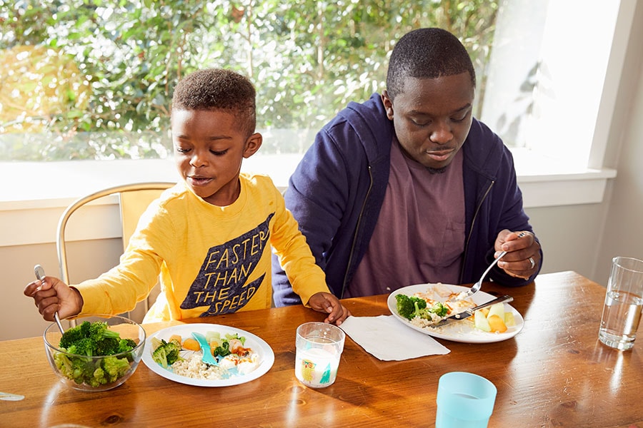 Toddler son serving himself at dinner while sitting next to dad