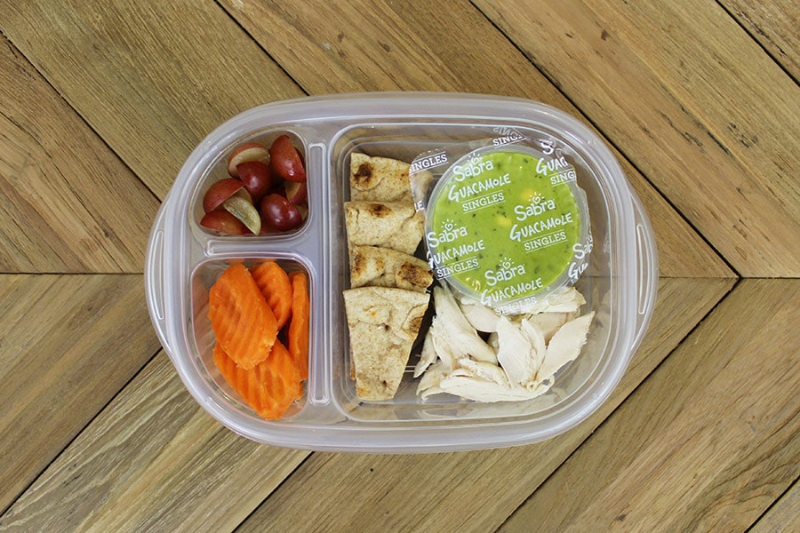 Bento lunch box with cut-up grapes, carrots, chicken, guacamole and pita bread for a packed toddler lunch