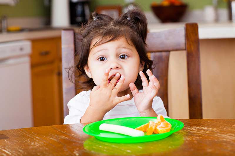 Niña pequeña comiendo con los dedos.