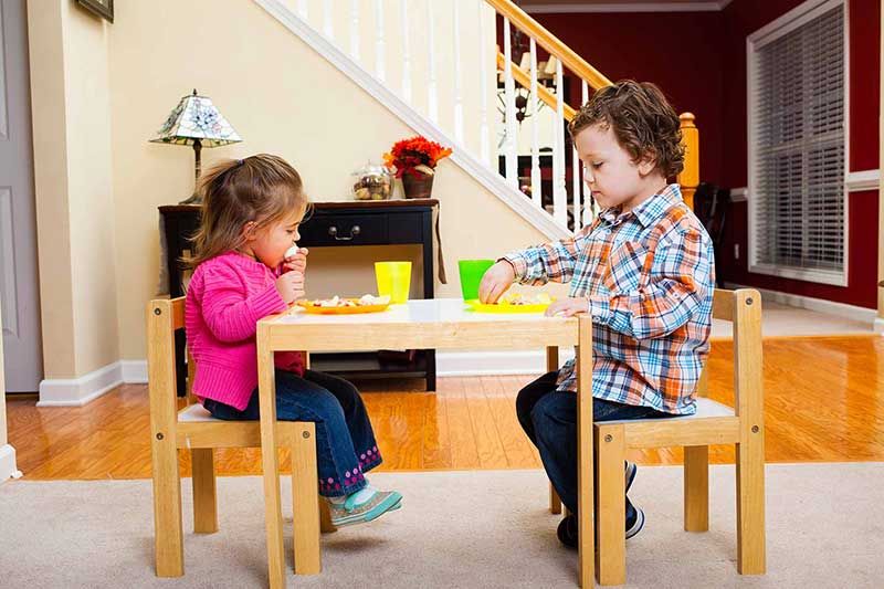 Un niño y una niña comiendo con los dedos en la mesa de los niños
