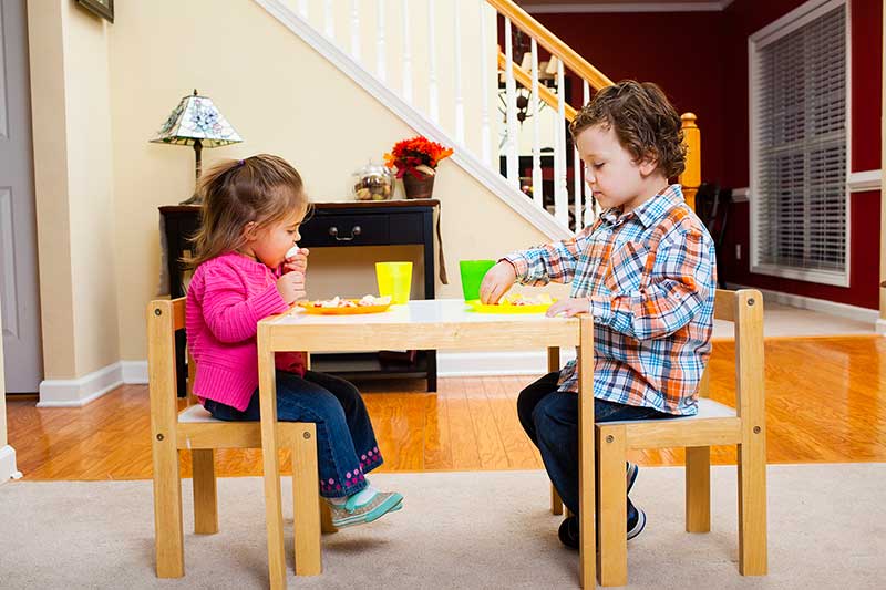 Dos niños comiendo una comida con los dedos en una mesa.