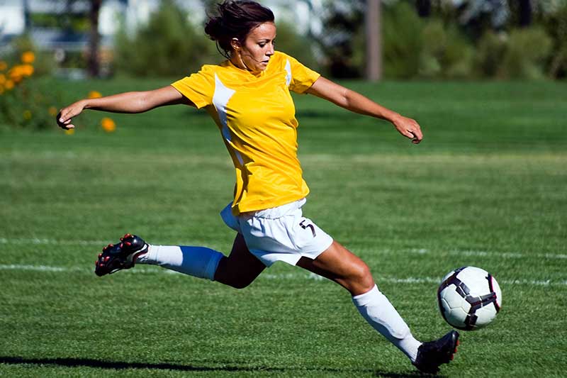 Teen girl playing soccer, kicking the ball