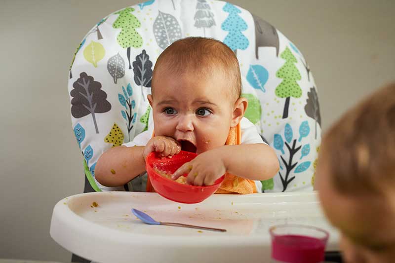 Bebé comiendo con los dedos de un tazón.