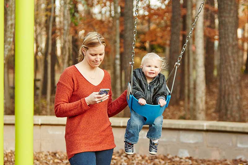 mom on phone with baby on swing