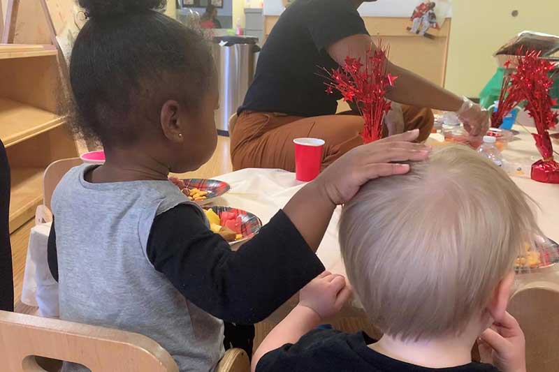 Black toddler girl patting the head of her white friend at daycare