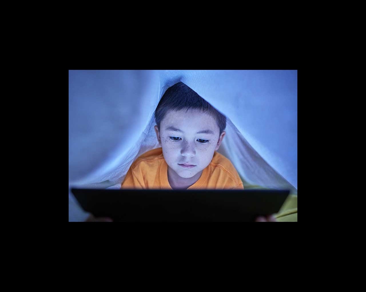 Young boy looking online under the covers